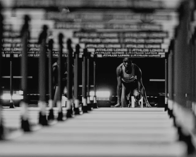 Hurdler settling into the blocks behind a row of ATHLOS London hurdles