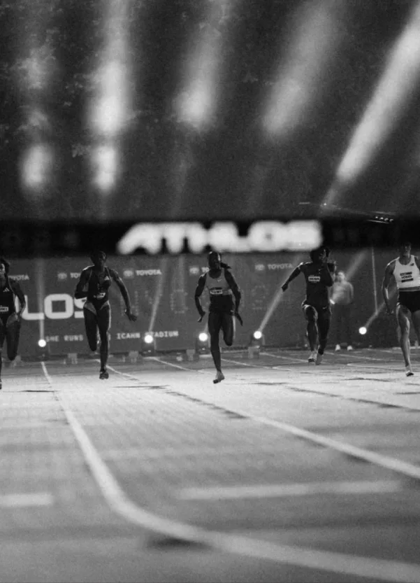 Sprinters racing towards the finish under the ATHLOS stadium lights